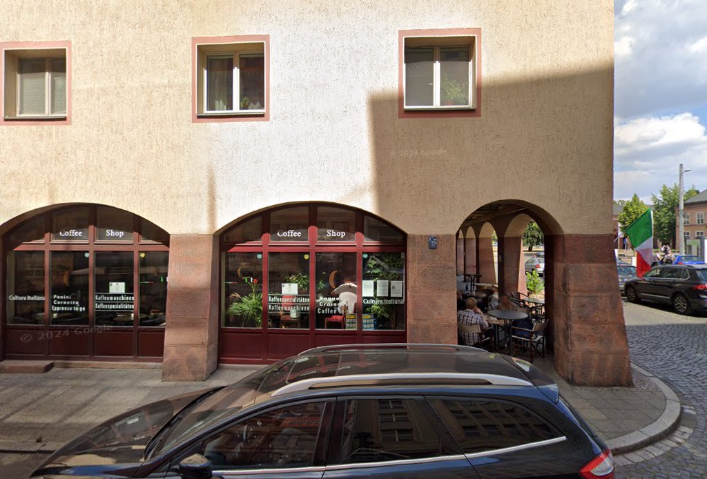 Außenansicht des Caffè d’Amici am Johannisplatz in Leipzig: Ladenfront mit Arkadeneingang und Terrasse